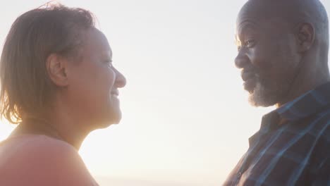 smiling senior african american couple looking at each other on sunny beach