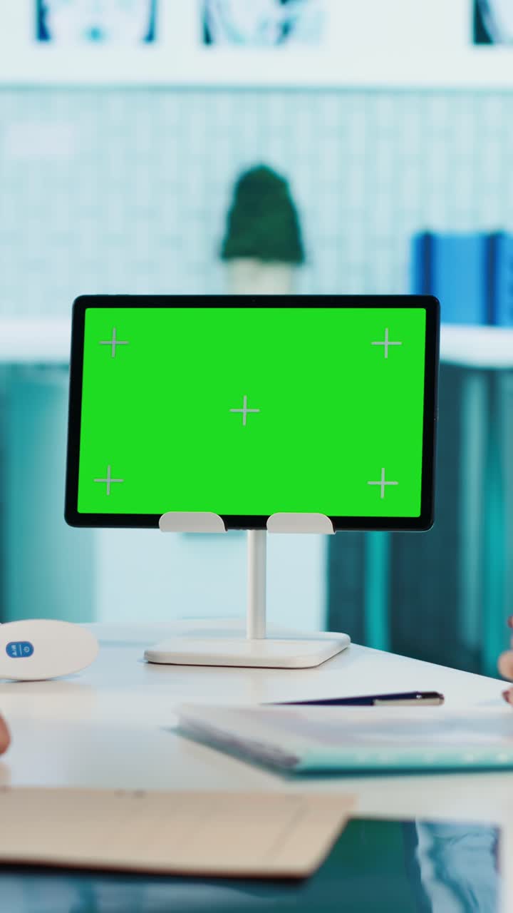 Tablet con schermo verde su scrivania d'ufficio con mani che gesticolano