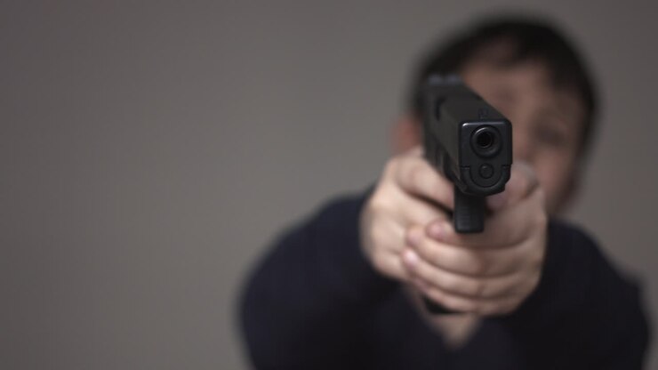 Silhouette sfocata di un ragazzino anonimo che punta una replica perfetta di una pistola giocattolo da nove millimetri verso la telecamera e spara