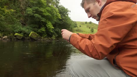 disparo de bajo ángulo de un pescador de mosca desenredando sus moscas en su línea a la orilla del río