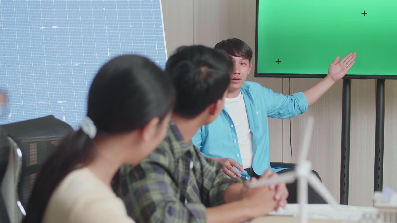 ingeniero asiático en silla de ruedas con célula solar presentando sobre la pantalla verde de la televisión en la oficina