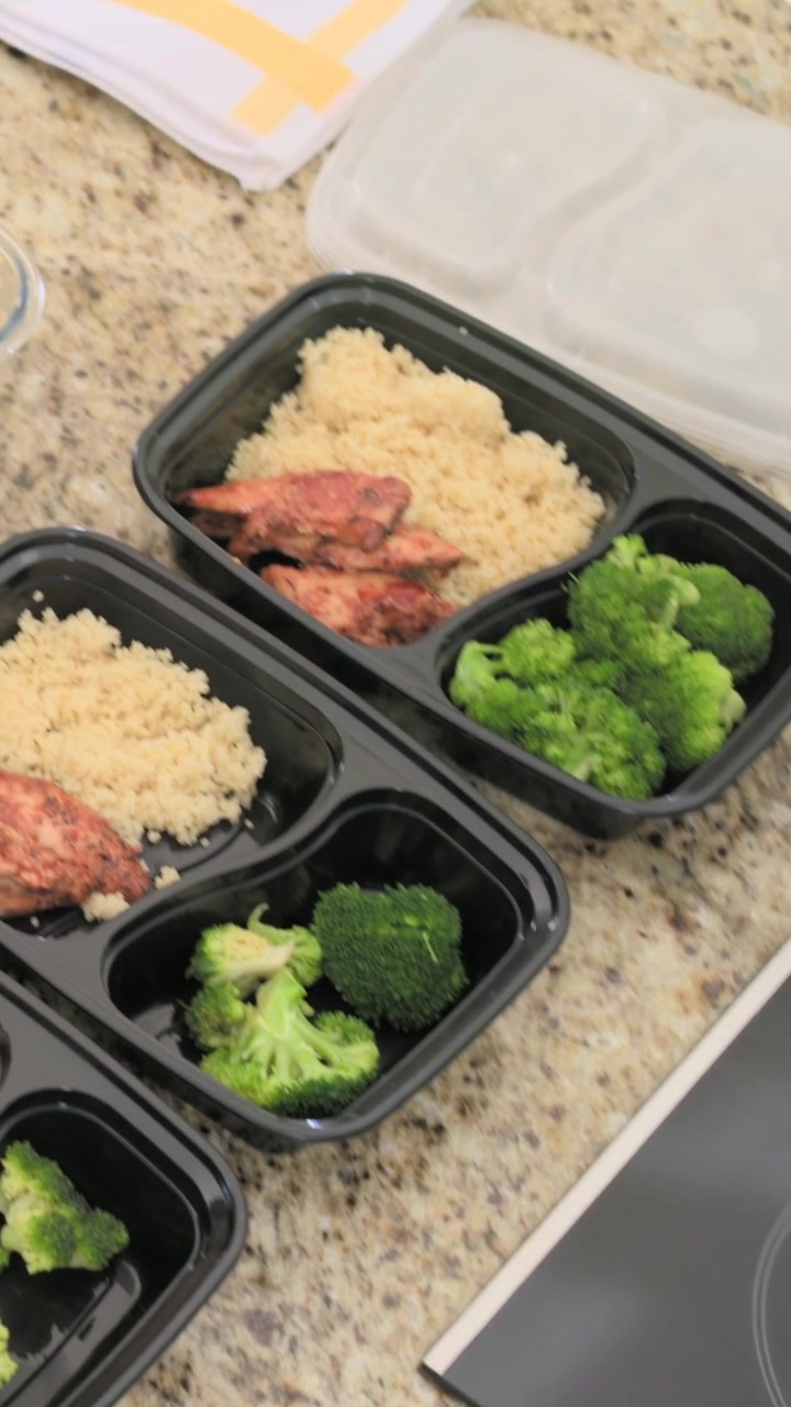 Video verticale: Mano che riempie vassoi con broccoli con un cucchiaio vicino ai fornelli per la preparazione dei pasti con riso, pollo