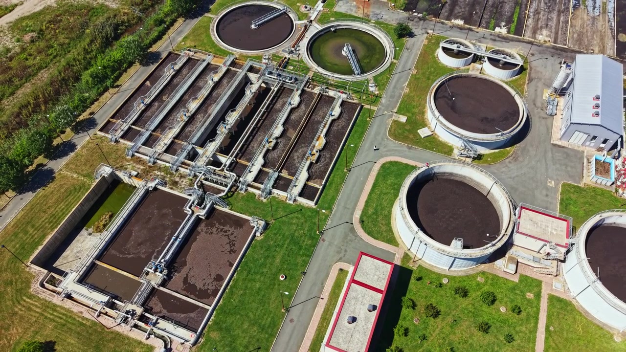 Water treatment facility located in a city processes wastewater with various tanks and machinery in clear view during daylight
