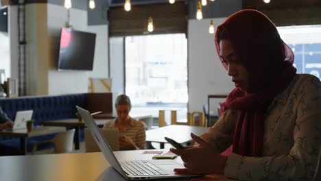 Woman-using-laptop-and-mobile-phone-in-cafe-4k