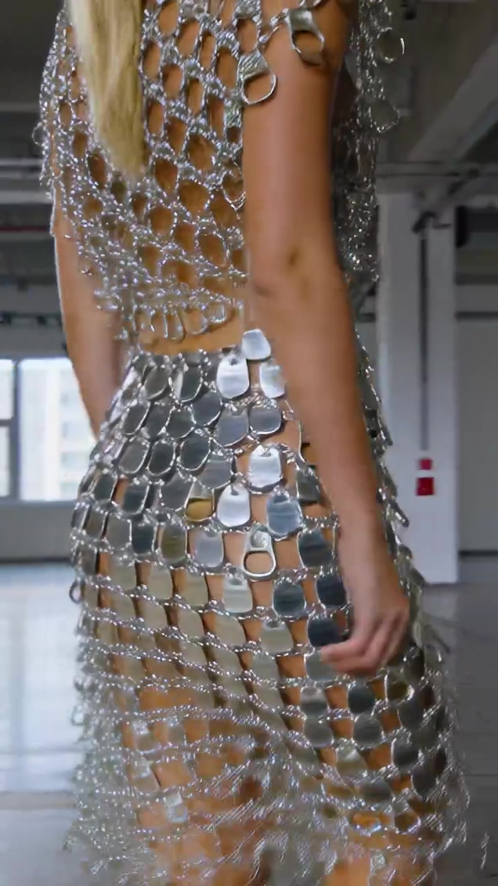 Video verticale: Modella bionda che cammina attraverso lo studio mostrando lo scintillio di un vestito con linguette metalliche collegate.