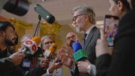 Female-politician-makes-an-announcement,-answers-journalists-questions-and-gives-interview-for-media.-Confident-representative-of-the-European-Union-during-press-conference.-Backdrop-with-EU-flags.