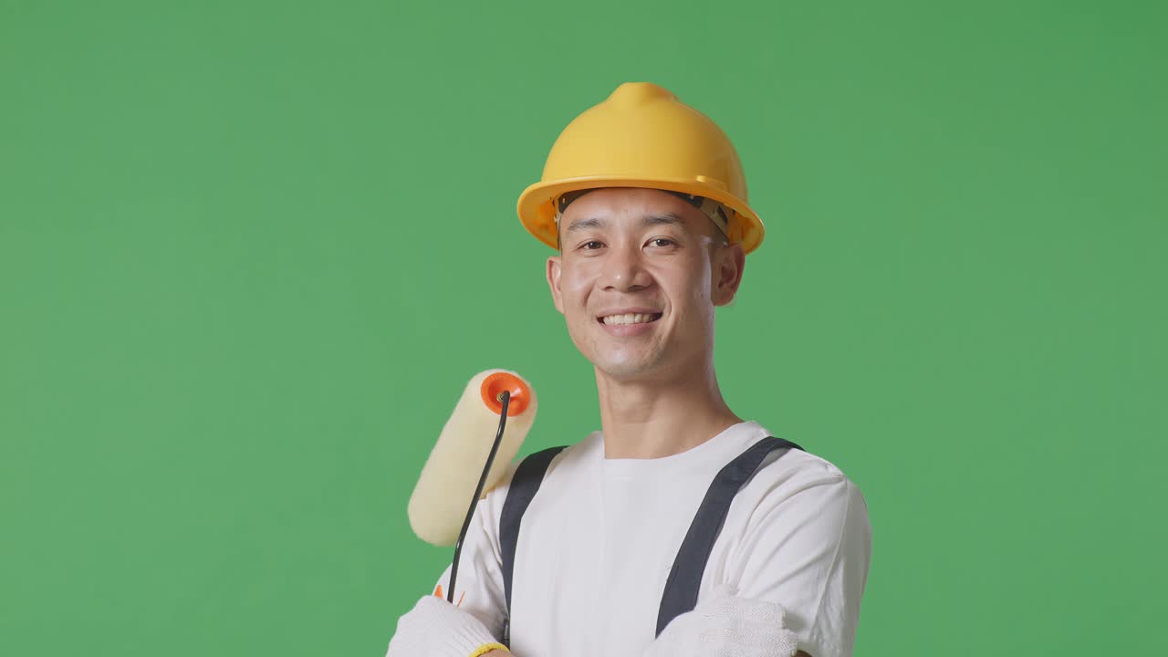 Close Up Side View Of Asian Man Painter Wearing Safety Helmet Smiling And Crossing His Arms While Standing In The Green Screen Background Studio