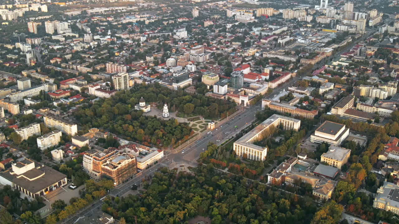 Aerial drone view of Chisinau downtown. Panorama view of multiple buildings, Central parks, roads with moving cars and lush trees. Sunset. Moldova