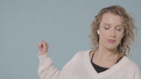 Close-Up-Shot-Of-Young-Woman-Listening-To-Music-On-Mobile-Phone-And-Dancing-Against-Blue-Background