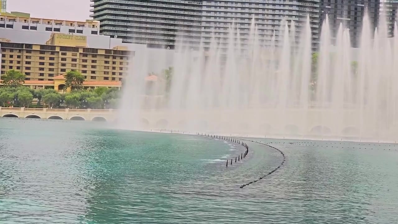 Espectáculo de fuentes de agua del Strip de Las Vegas con chorros curvos, reflejos en el lago, arcos de piedra, árboles, hoteles de gran altura y paisaje soleado del resort para videos de viajes y turismo