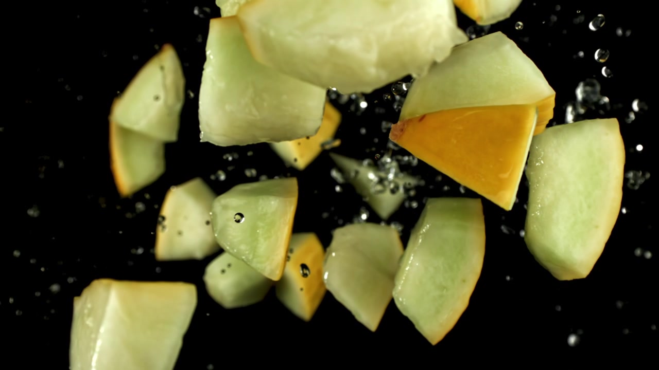 Juicy Melon Chunks Falling and Splashing with Water on Black Background