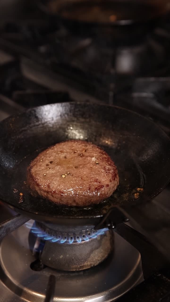Hamburgare som steks i en panna på en gasspis.