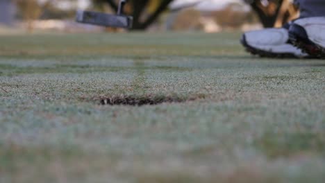 Golfer-putts-and-drops-ball-into-hole,-point-of-view-from-behind-hole-and-slow-motion