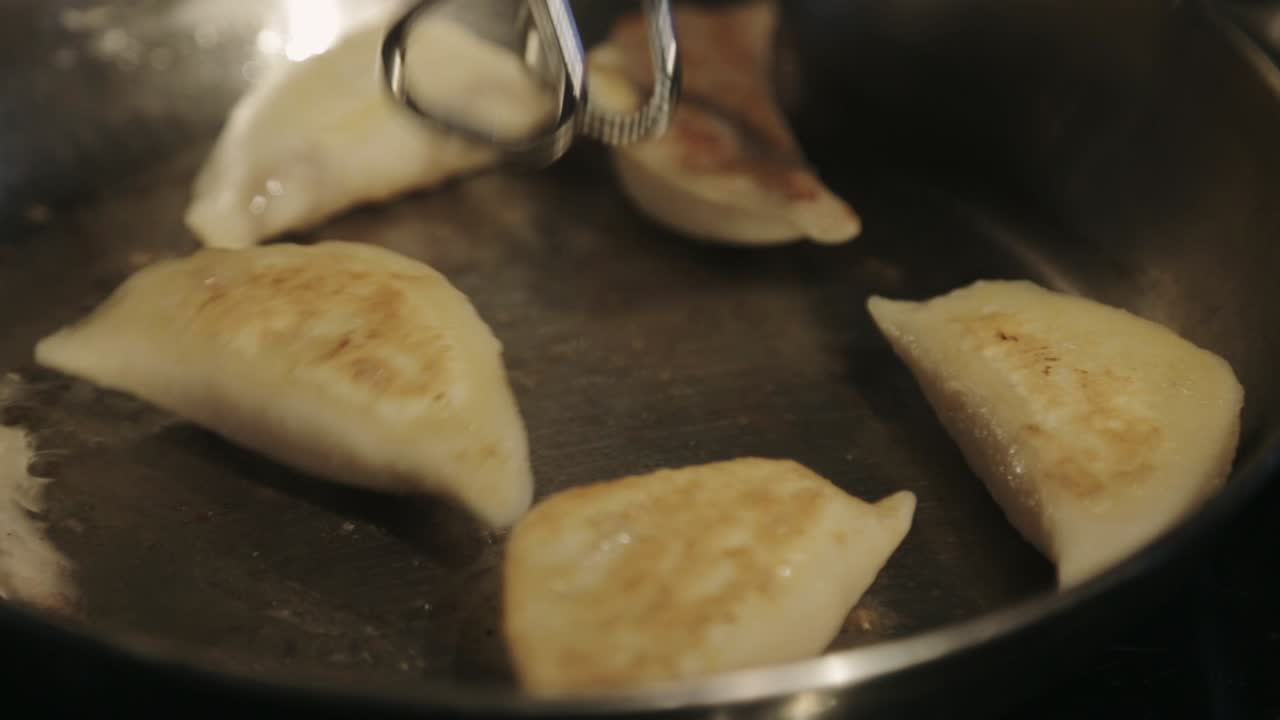 Canada - Frying Delicious Dumplings In A Stainless Pan Using Tongs To Turn Over - Closeup Shot