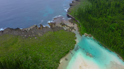 toma de drones de una separación entre una piscina natural con una playa y el océano rompiendo son olas en la costa rocosa creando un patrón de espuma