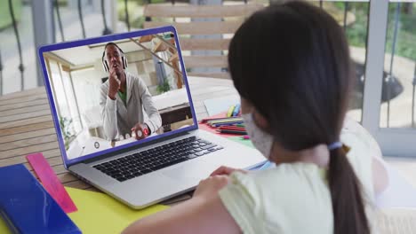 Caucasian-girl-wearing-face-mask-having-a-video-call-on-laptop-at-home