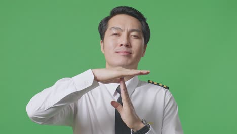 close up of asian man pilot looking at camera and showing time out hands gesture while standing in the green screen background studio