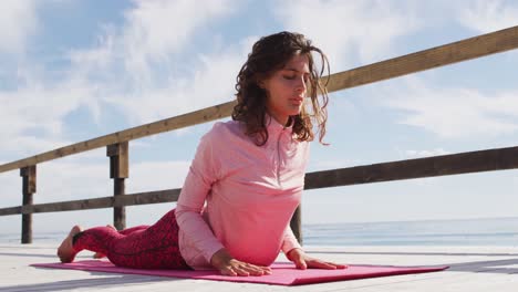 mujer de raza mixta practicando yoga saludable al aire libre, acostada y estirándose con los ojos cerrados por el mar