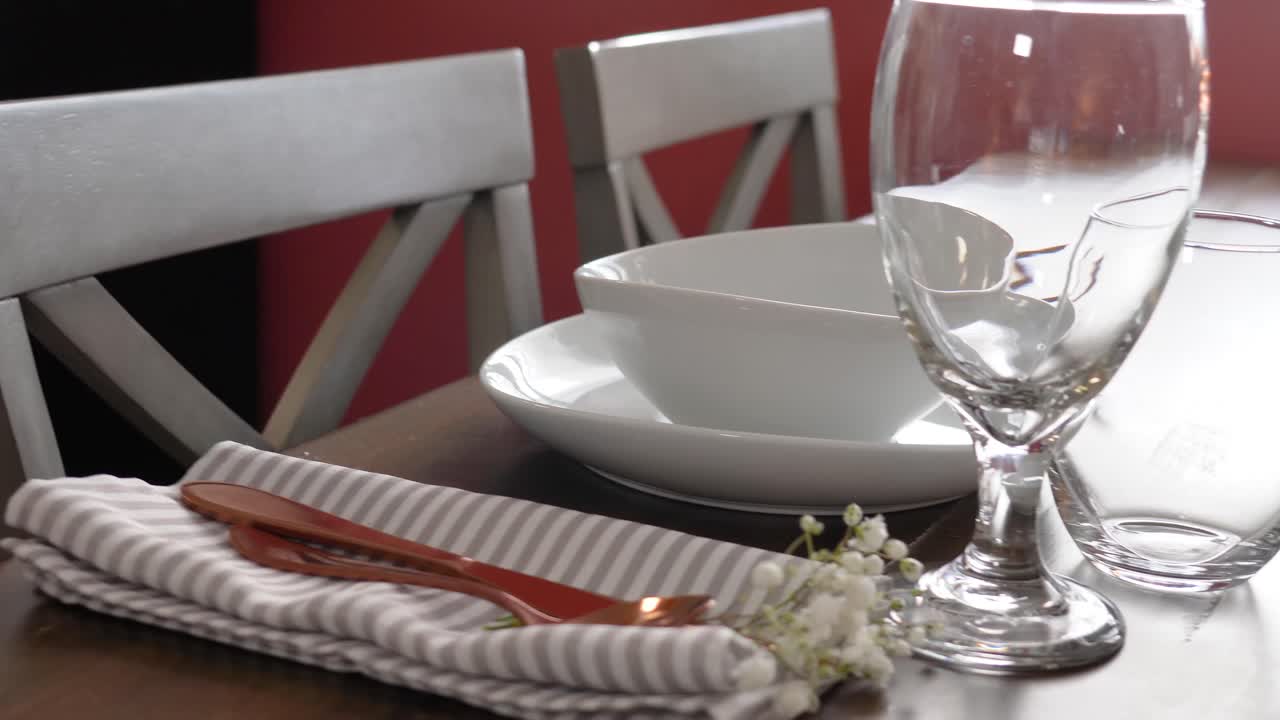 Romantic Dining Room Table Set for Dinner with White Plates and Wine Glasses with Beautiful Flowers and Lit Candels next to Sunny Window, Gimbal Pan Right Movement, Forks, Knives and Napkins