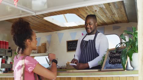 smiling african american male food truck owner taking order from happy female customer