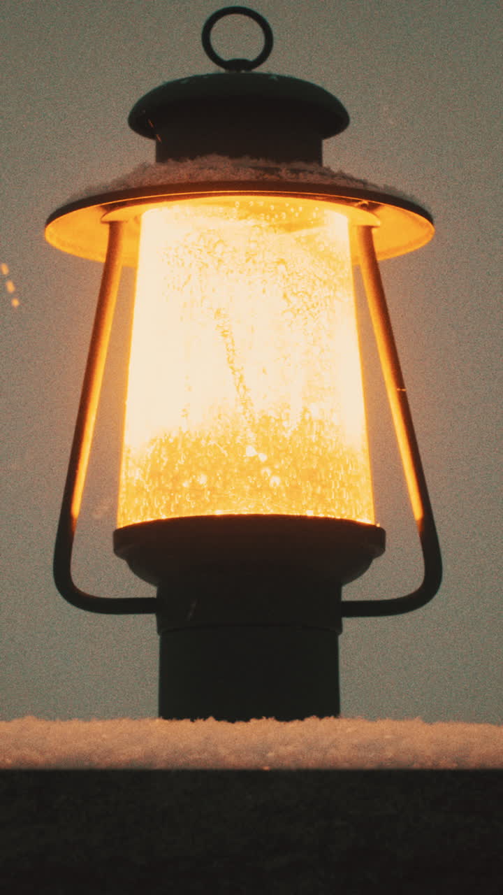Scatto verticale di un lampione posto su una colonna di cemento che illumina con una luce gialla mentre nevica al crepuscolo