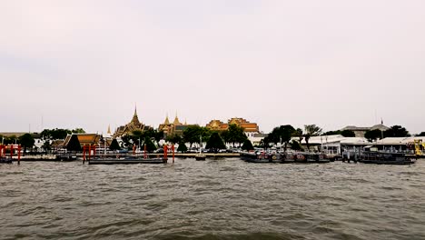 La-Animada-Escena-Del-Río-Bangkok-Con-Barcos-Y-El-Gran-Palacio-En-La-Distancia,-El-Día-Nublado,-El-Gran-Palacio-En-La-Parte-Trasera