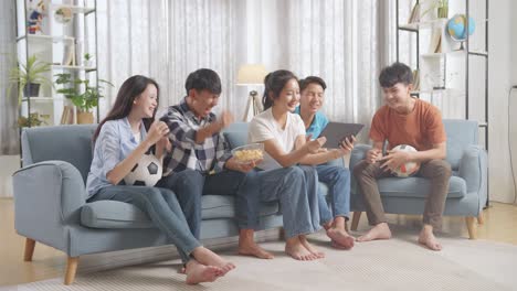 asian teenagers cheering and watching football game on tablet and celebrating victory at home