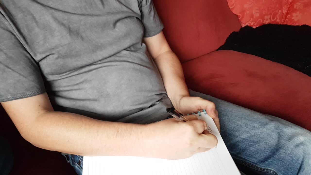 Male with a partially amputated index finger on his right hand sat down holding a pen and pad  writing a to do list.