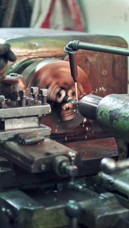 a worker controls the process of drilling a hole in a part on a lathe using coolant for cleanliness processing of surface. close-up. vertical video