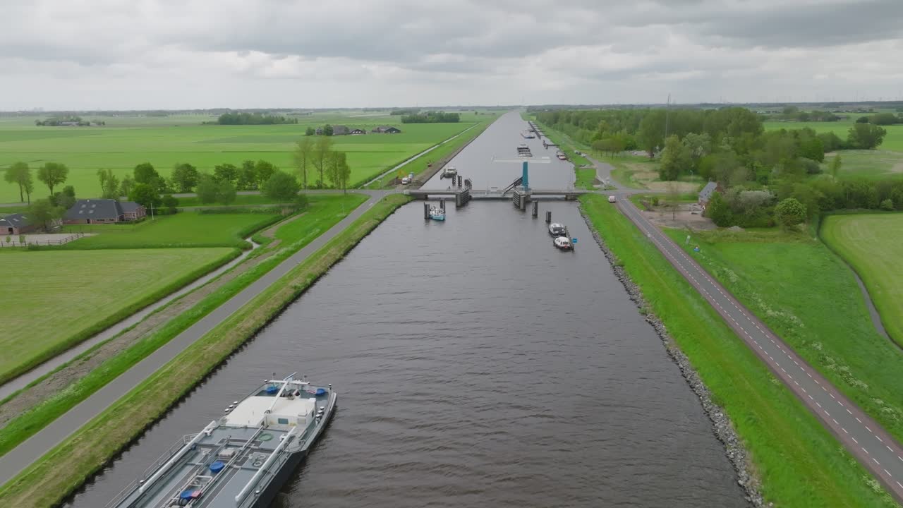 A tanker barge transits a straight canal bordered by cycle paths and farmland in the Dutch countryside