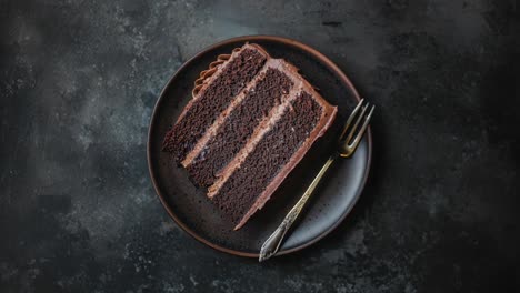 a slice of decadent chocolate cake with chocolate frosting on a dark brown plate with a fork