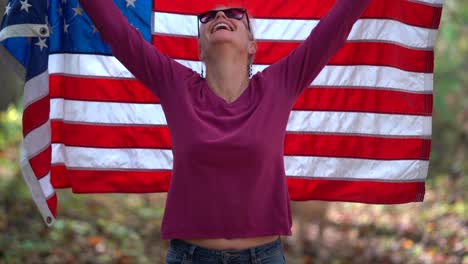 blonde woman raising an american flag behind her with smiling expression