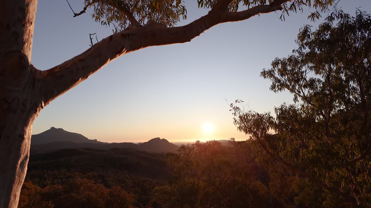 el lapso de tiempo de la puesta de sol a través de árboles y montañas siluetadas