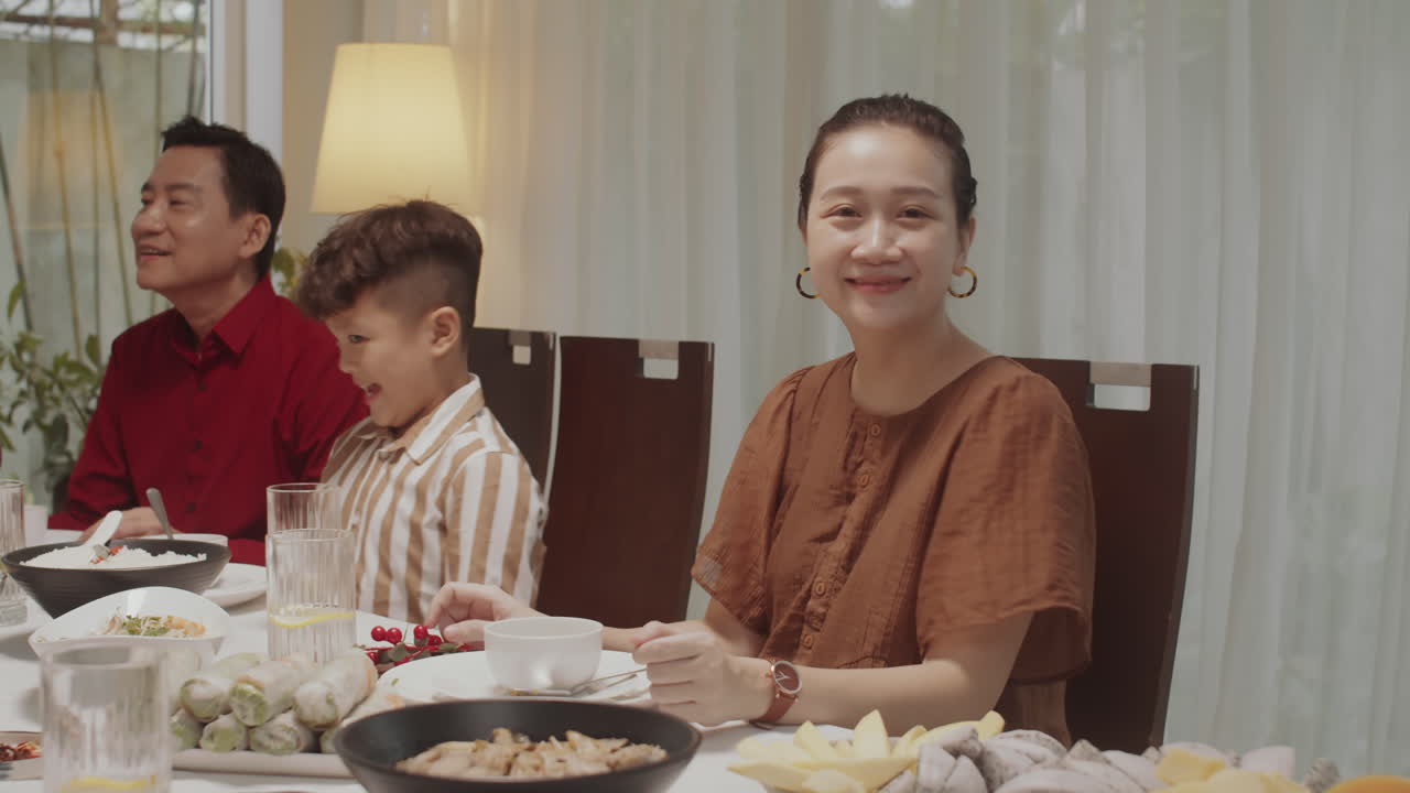 Asian Woman Smiling at Camera at Dinner Table with Family