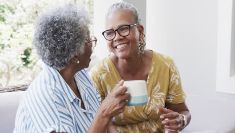 Felices-Amigas-Afroamericanas-Mayores-Tomando-Café-Y-Riendo-En-La-Sala-De-Estar,-Cámara-Lenta