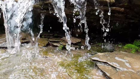 low-angle-Slow-motion-footage-of-Small-waterfall-mountain-spring-stream-running-down-huge-sandstone-slabs-of-rock-with-green-moss,-crystal-clear-drinking-water,-meditate-tranquil-and-peaceful