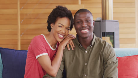 video of happy african american couple sitting on sofa and looking at camera