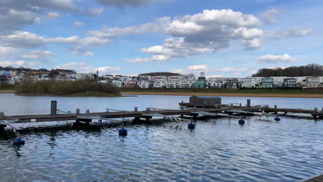 pan shot of wooden dock of phoenix lake in dortmund with luxury villas on shore in background