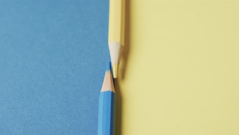 Close-up-of-yellow-and-blue-crayons-with-copy-space-on-blue-and-yellow-background,-in-slow-motion