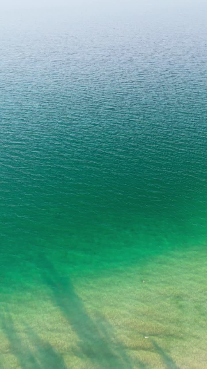 Ocean Ripples, calm turquoise water surface sparkling with green golden light. Vertical Aerial top down shot, 4K