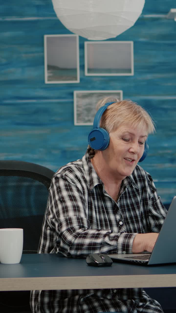 Vertical video: Happy old woman with headset listening music while checking statistics,