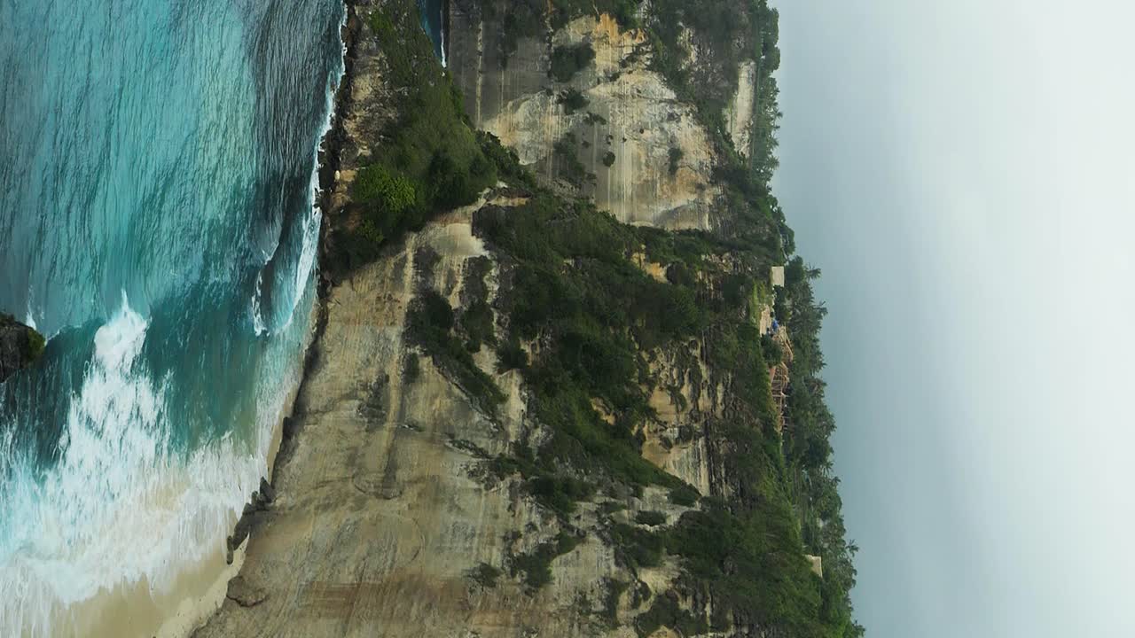 panorama vertical en cámara lenta tomado desde la impresionante playa de diamantes en nusa penida, bali, que ofrece una hermosa vista de los imponentes acantilados y el mar azul, adornado por las ondas rítmicas