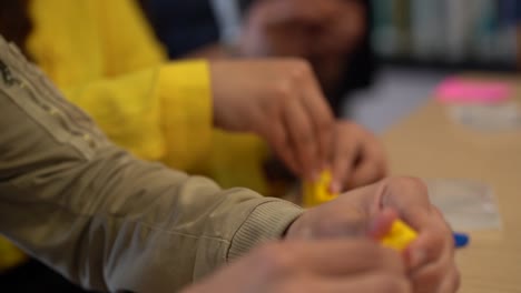 los dedos de los hombres caucásicos ensamblan ladrillos de plástico amarillos entrelazados, en cámara lenta