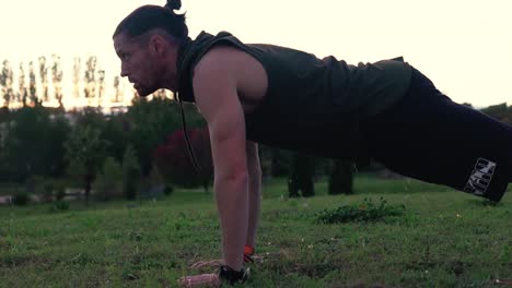 a muscular sportsman is doing push-ups in a park, with the sunset behind