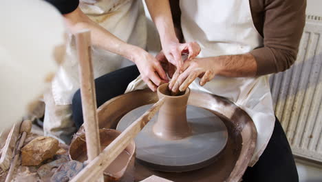 close up of male teacher helping man sitting at wheel in pottery class