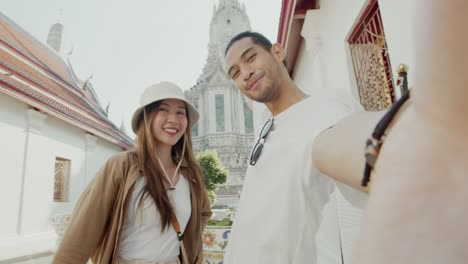 happy asian couple tourist take selfie and video call at wat arun in thailand.