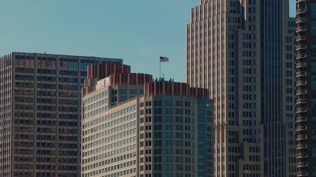 Arranha-céus do centro de Chicago subindo em um céu azul aberto com uma bandeira nacional hasteada — uma metáfora visual para poder corporativo, ambição e força econômica