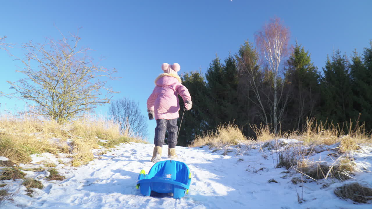 niña vista desde atrás subiendo una colina cubierta de nieve con trineo