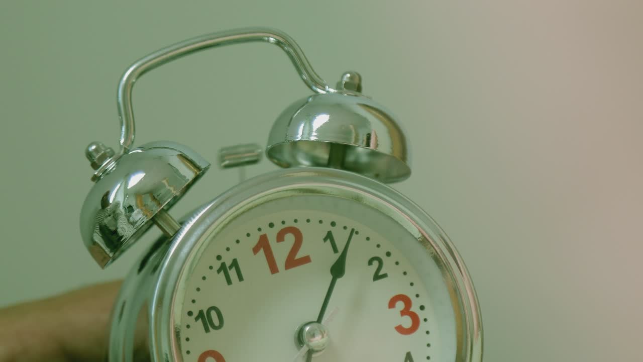 el reloj despertador a la vieja moda suena por la mañana en una mesa. la mano de la niña invierte la alarma para que se cierre. la niña dormida se despierta de la alarma llamando y apagándola.