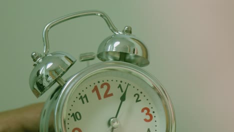 old fashioned alarm clock rings in the morning on a table . girl’s hand overturns the alarm so that it shuts up . sleeping girl waking up from alarm calling and turning it off . classic clock ringing